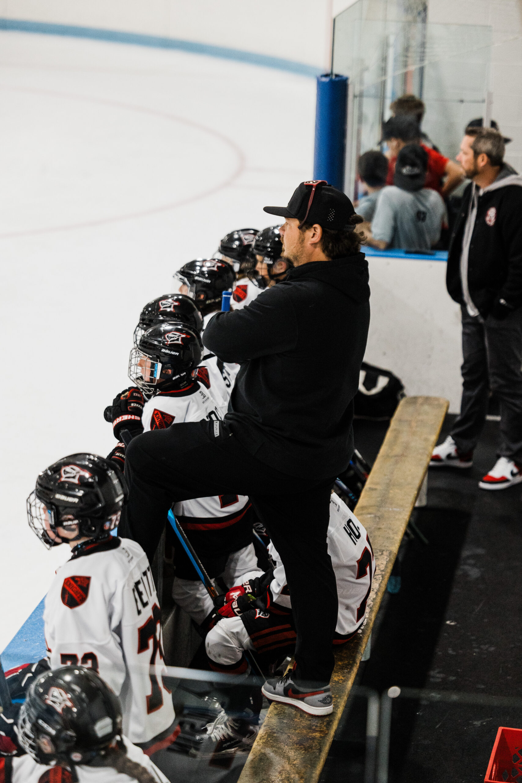 Jake Javitt standing on the bench with one foot up, watching a youth hockey game from behind his players