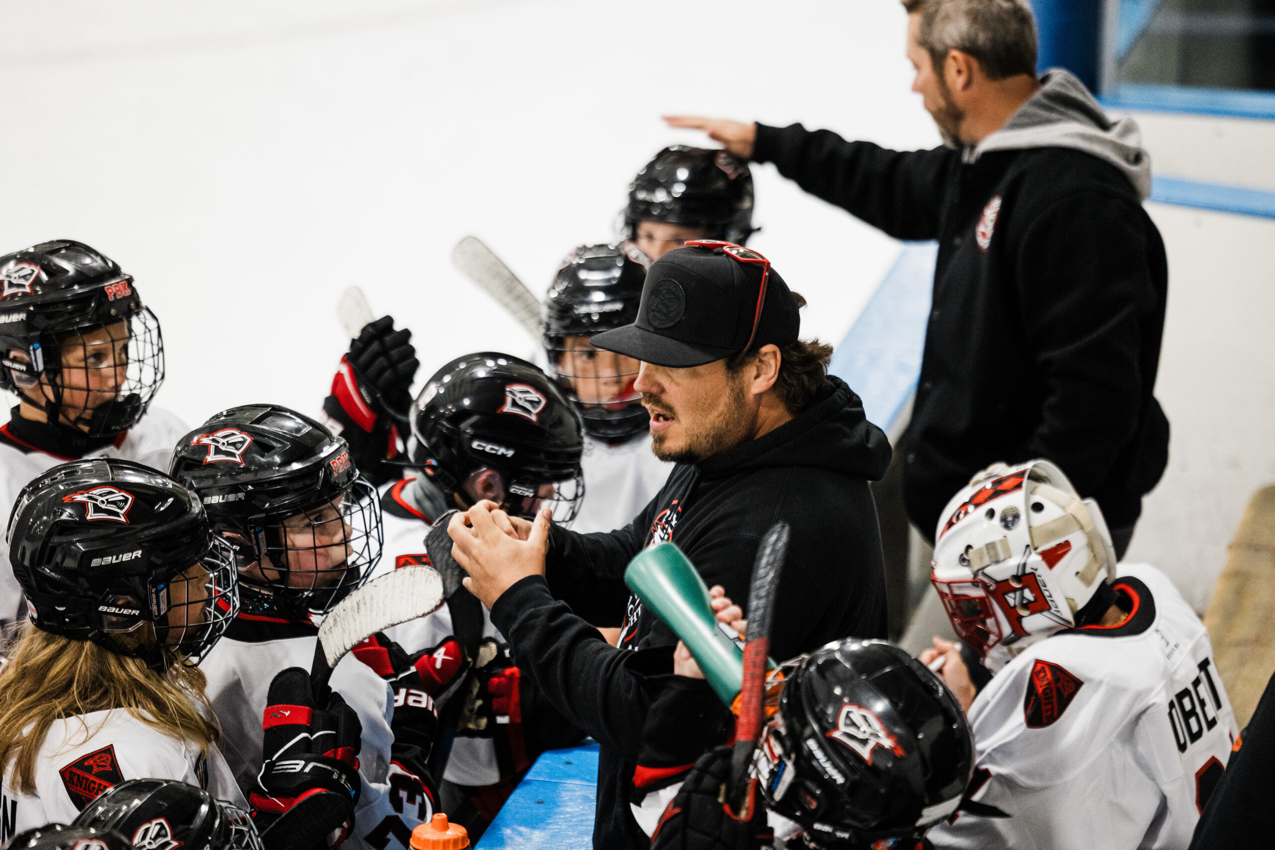 Coach Jake Javitt using his hands to explain a play to youth hockey players at the bench