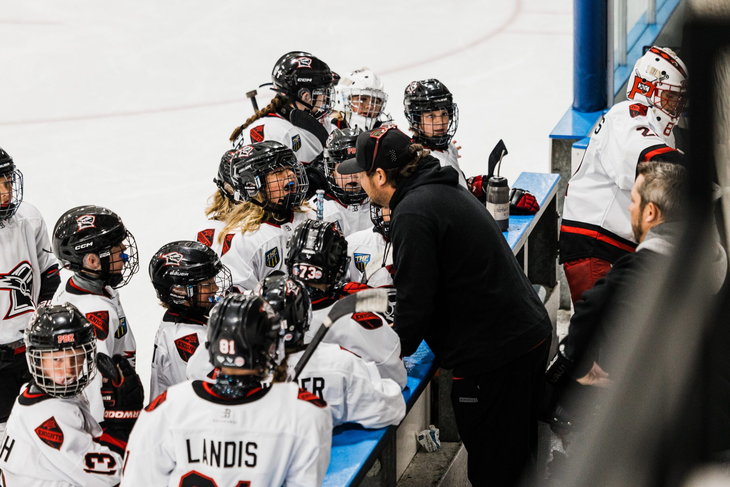 Jake Javitt leaning in to coach youth players gathered around him at the bench